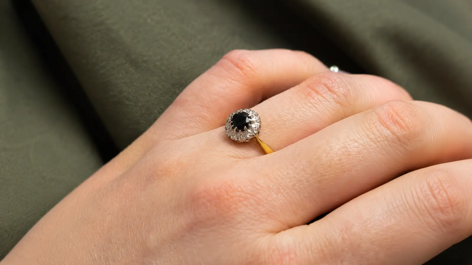 A hand wearing a black halo engagement ring with a dark center gemstone framed by a sparkling halo setting