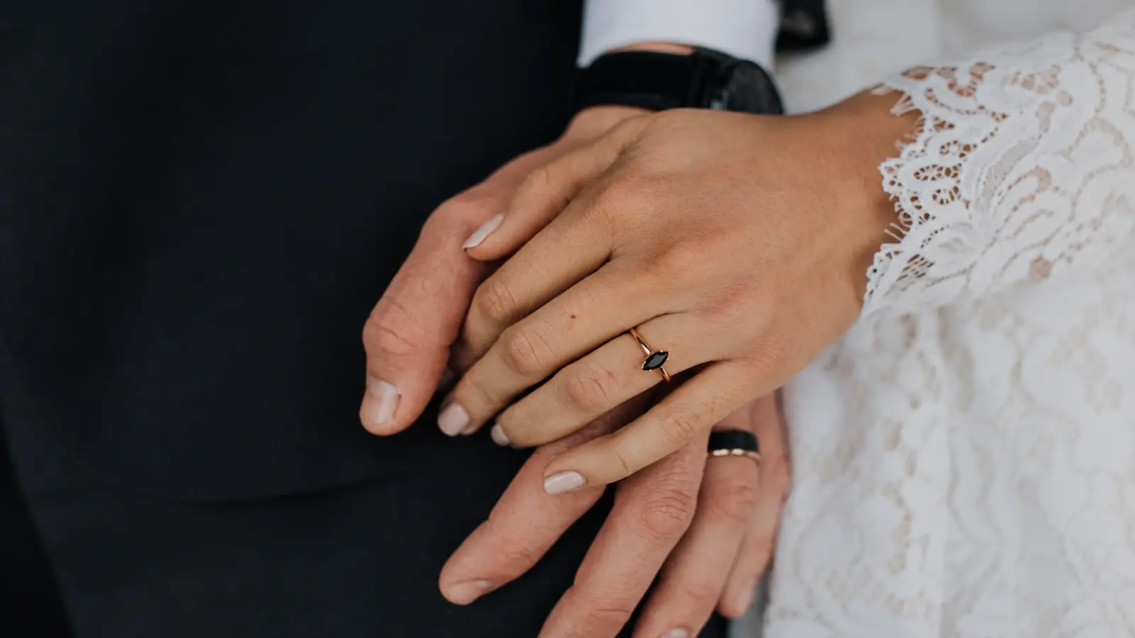 Bride and groom holding hands while showcasing a black marquise wedding ring and coordinating modern wedding bands