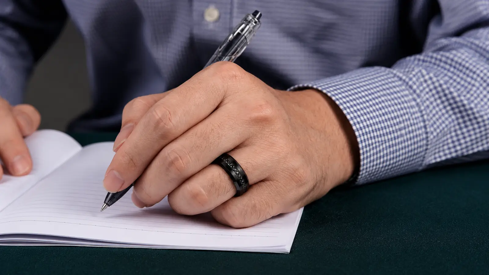 Man writing in a notebook while wearing a black men's diamond wedding band with subtle black diamond accents