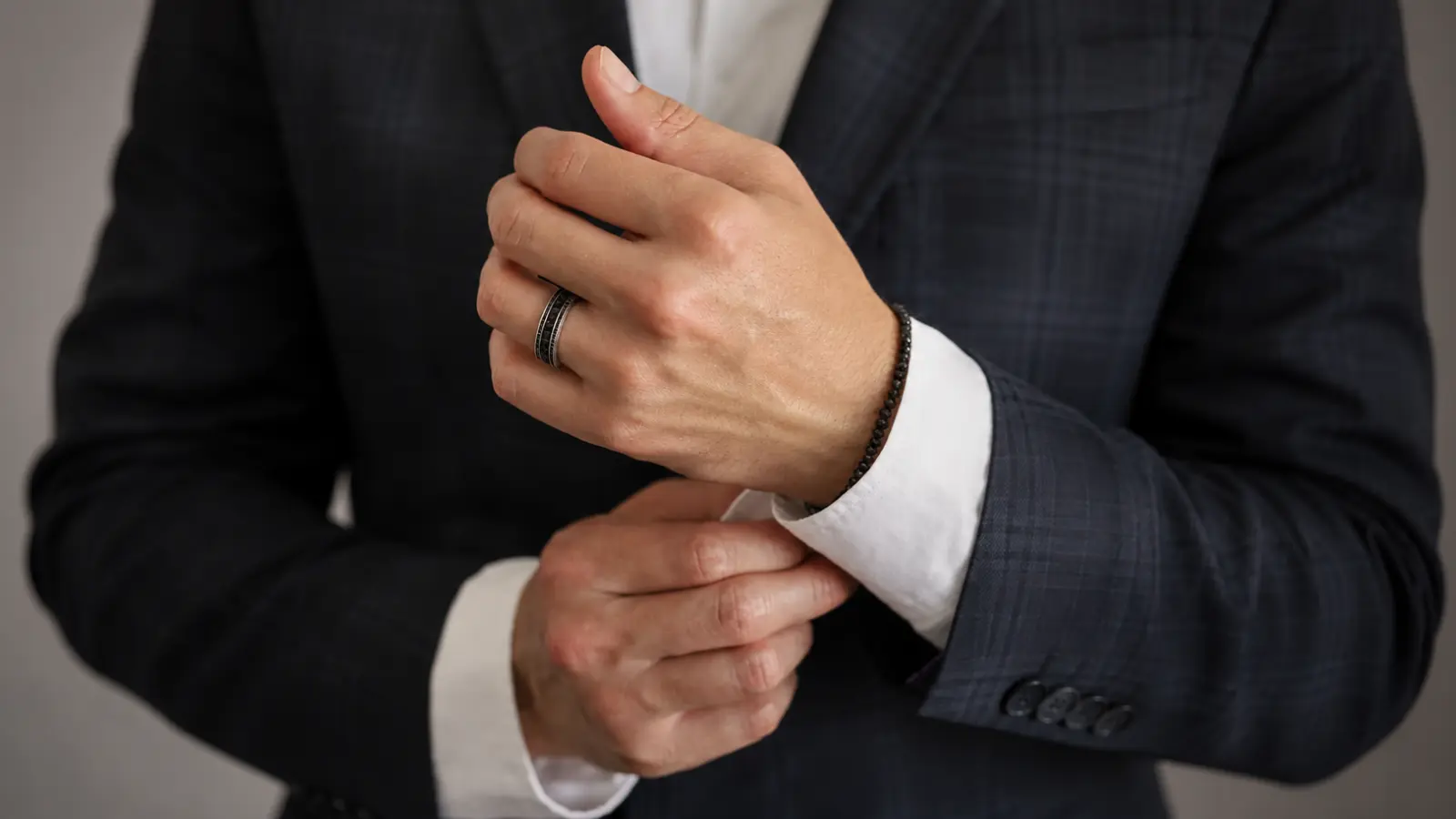 Close-up of a groom adjusting his cuff while wearing a black tungsten men's wedding ring with a tailored navy suit, highlighting a sleek modern wedding band