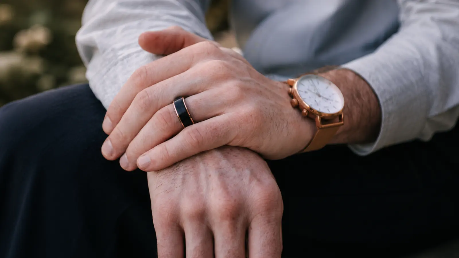A man wearing a black tungsten wedding ring with rose gold accents rests his hands together, highlighting the ring's contemporary masculine style