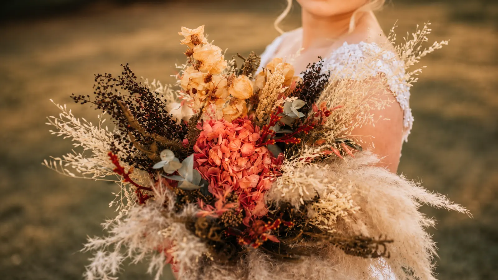 Bride holding a boho fall wedding bouquet with dried flowers, pampas grass and preserved autumn botanicals