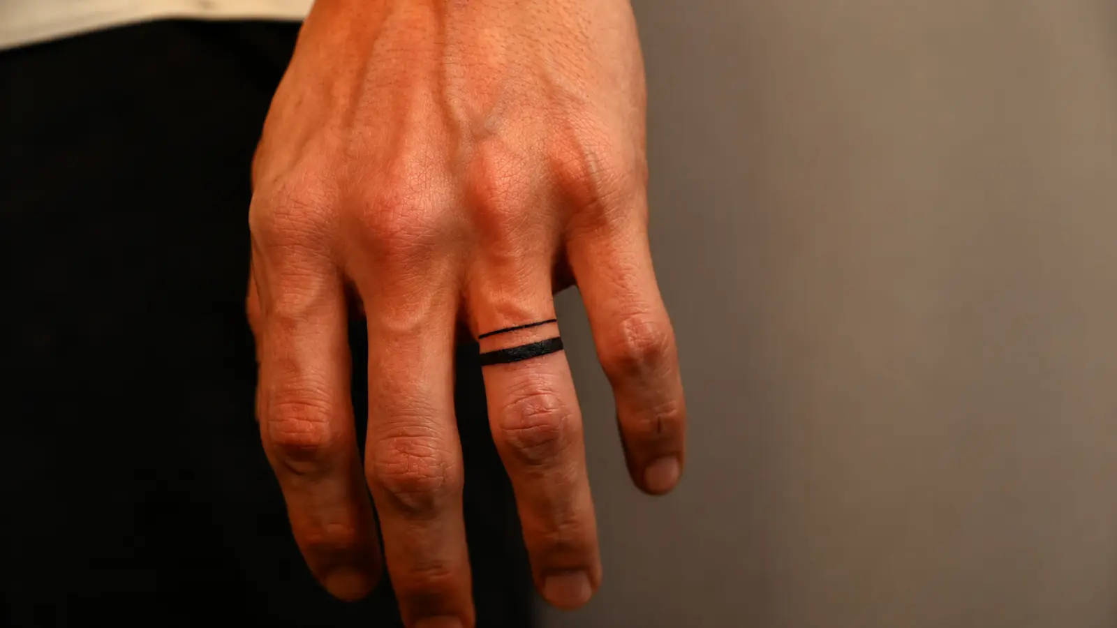 Close-up of a bold black wedding band tattoo on a ring finger
