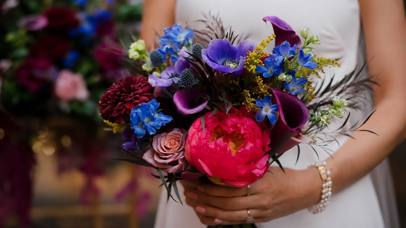 Bride holding a bold colorful wedding bouquet with blue delphiniums, purple calla lilies and pink peonies