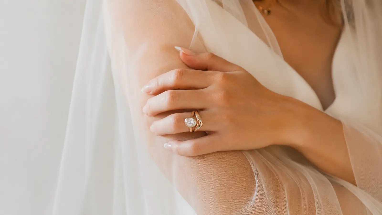 A bride gently rests her hand on her arm while wearing a diamond wedding ring featuring a prominent center stone and elegant bridal styling