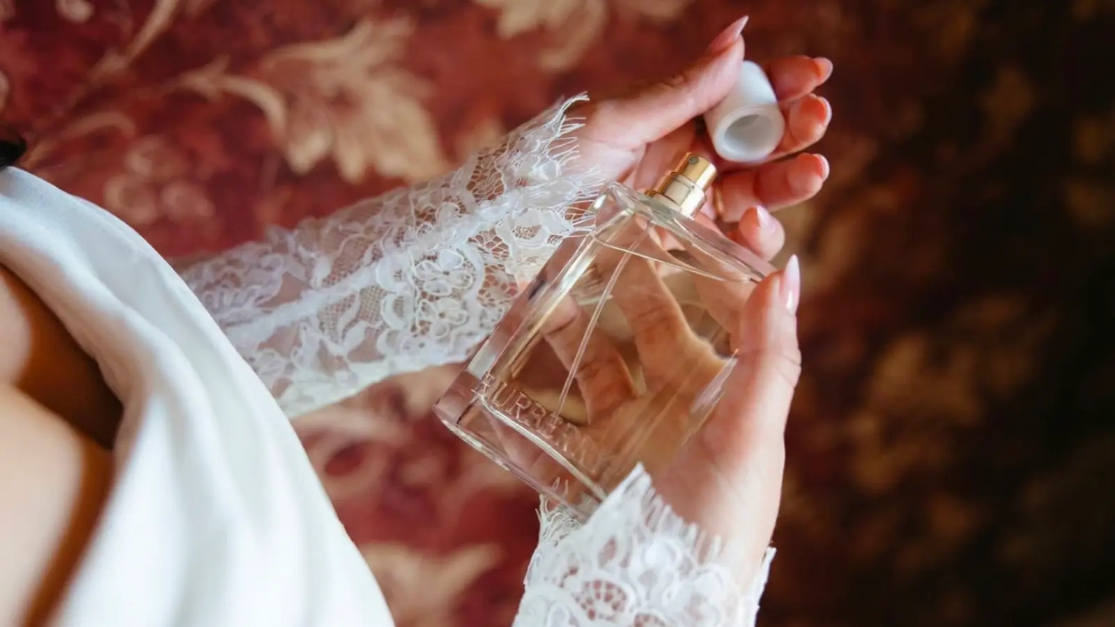 A bride opening a luxury bridal perfume bottle before applying her signature fragrance, completing the final steps of her wedding morning beauty routine with an elegant and memorable scent