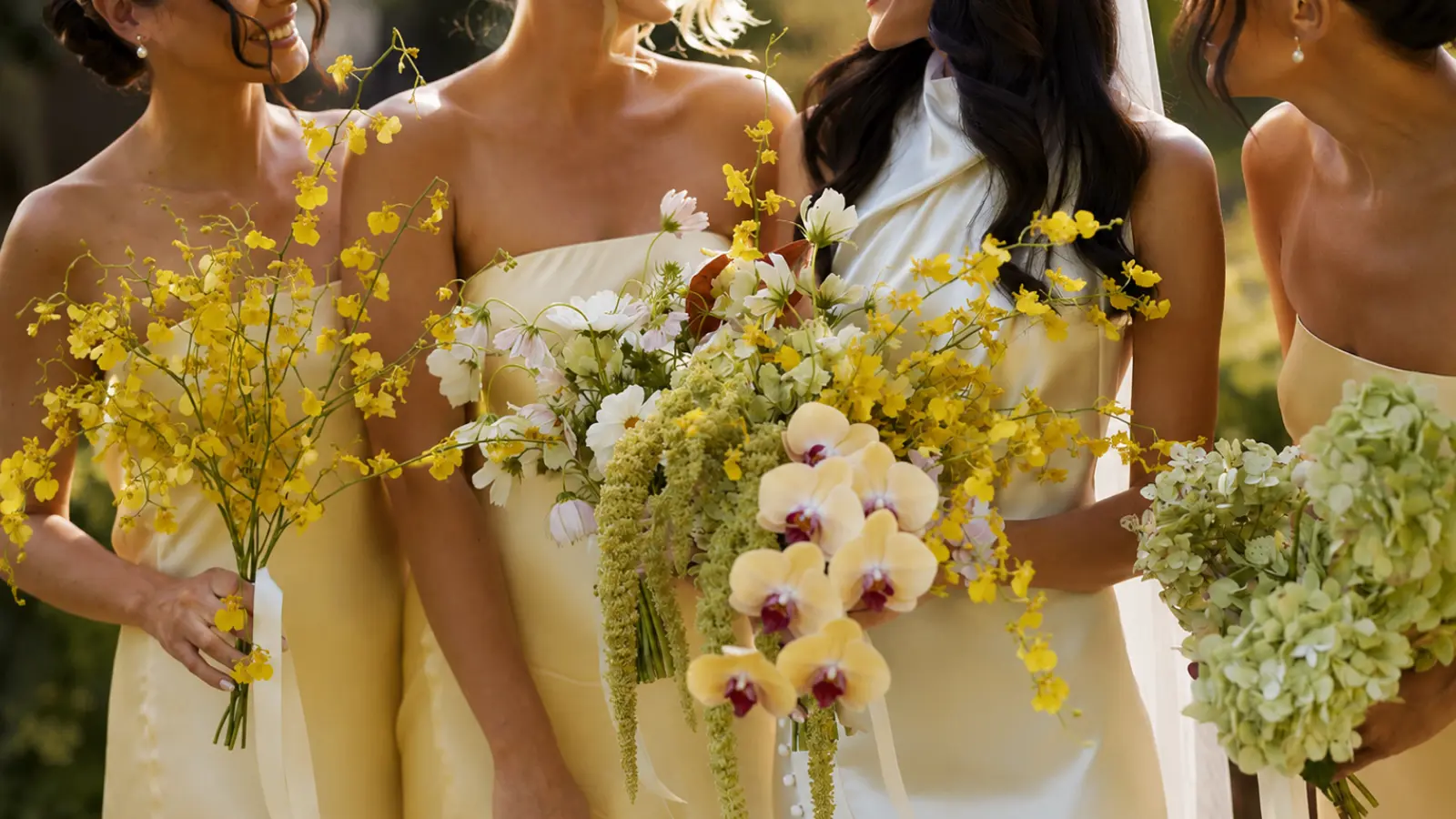 Bridesmaids holding yellow orchid wedding bouquets with hydrangeas, white flowers, trailing greenery, and soft yellow dresses