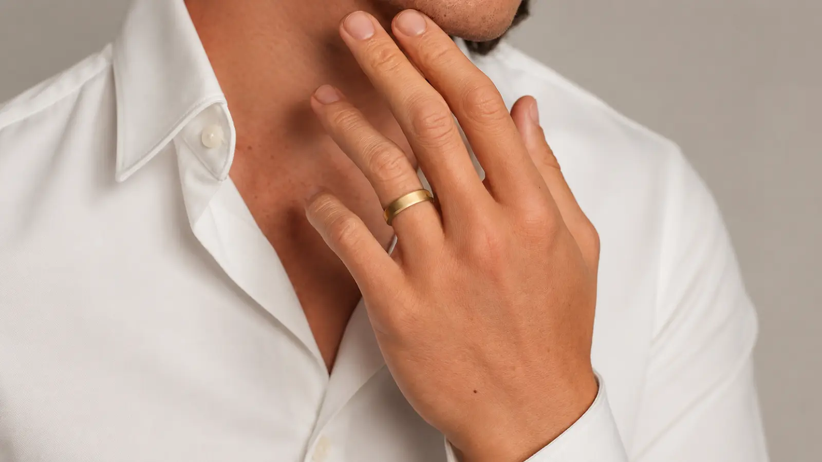 A man wearing a brushed modern gold wedding band with a flat profile and minimalist matte finish against a white shirt