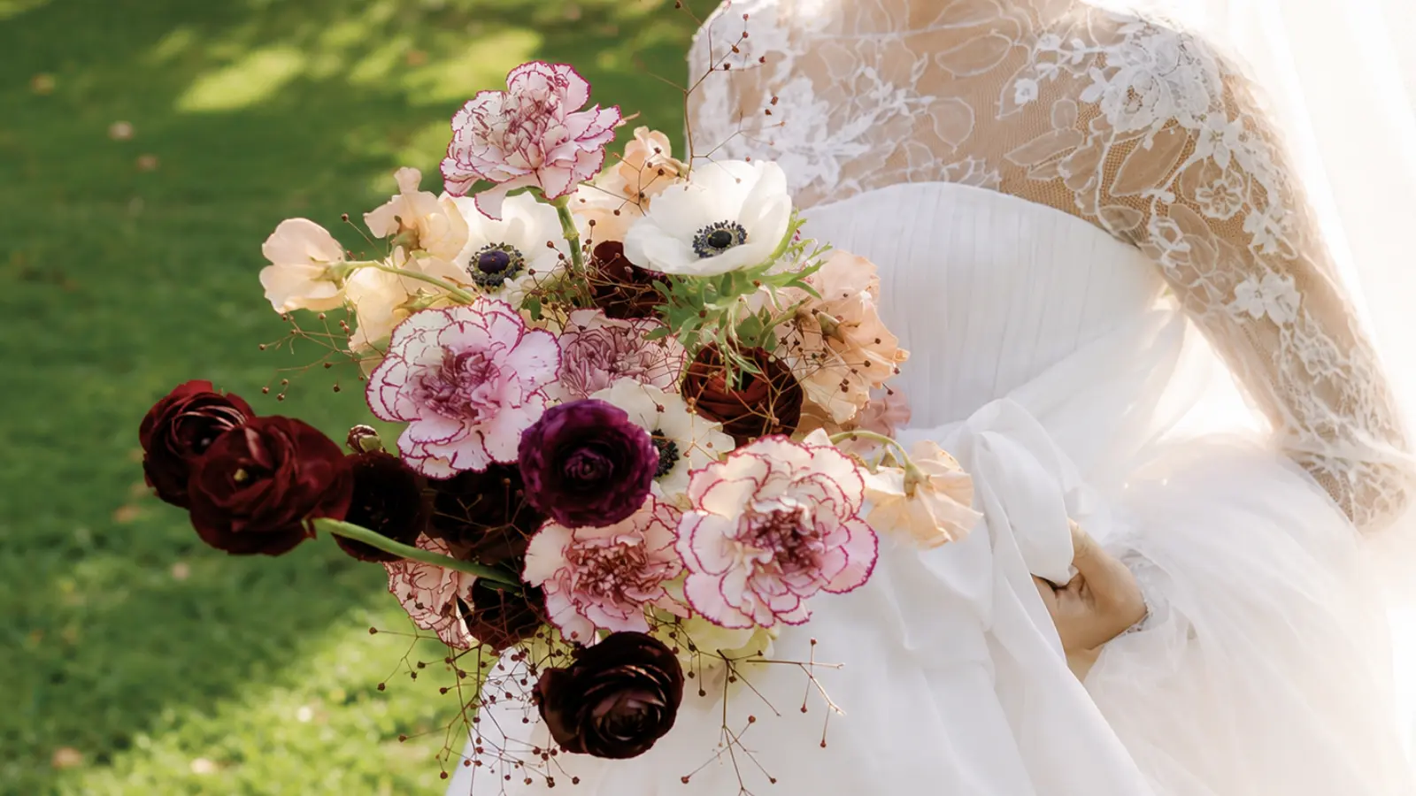 Bride holding a burgundy and cream wedding bouquet featuring ranunculus, anemones and soft garden flowers