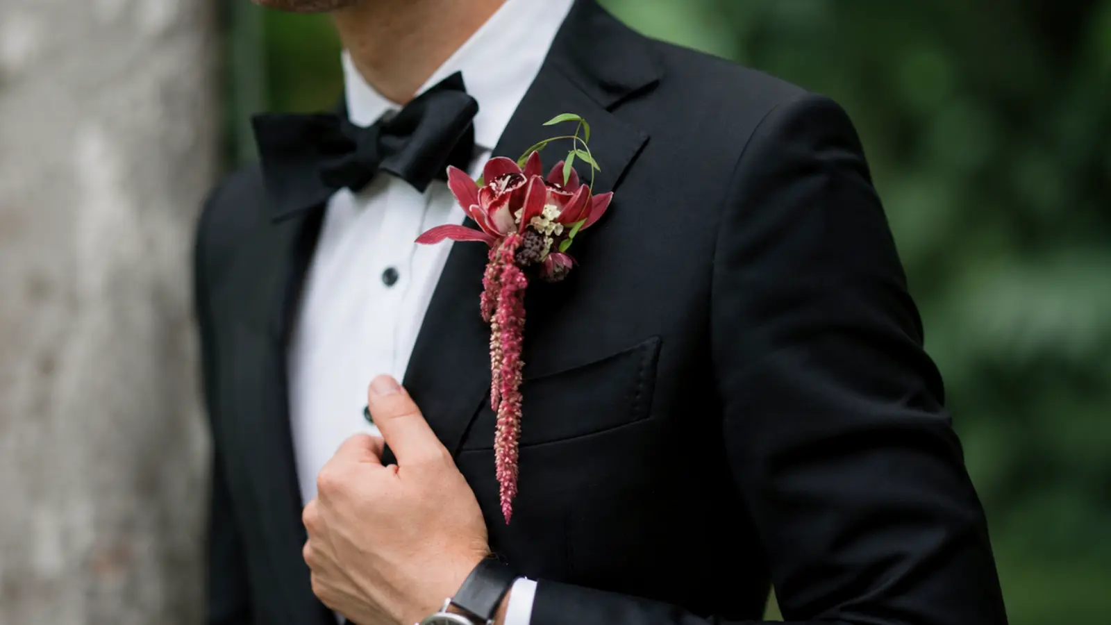 Groom in a black tuxedo wearing a burgundy orchid wedding boutonniere with trailing flowers Wedding Bouquet and Boutonniere