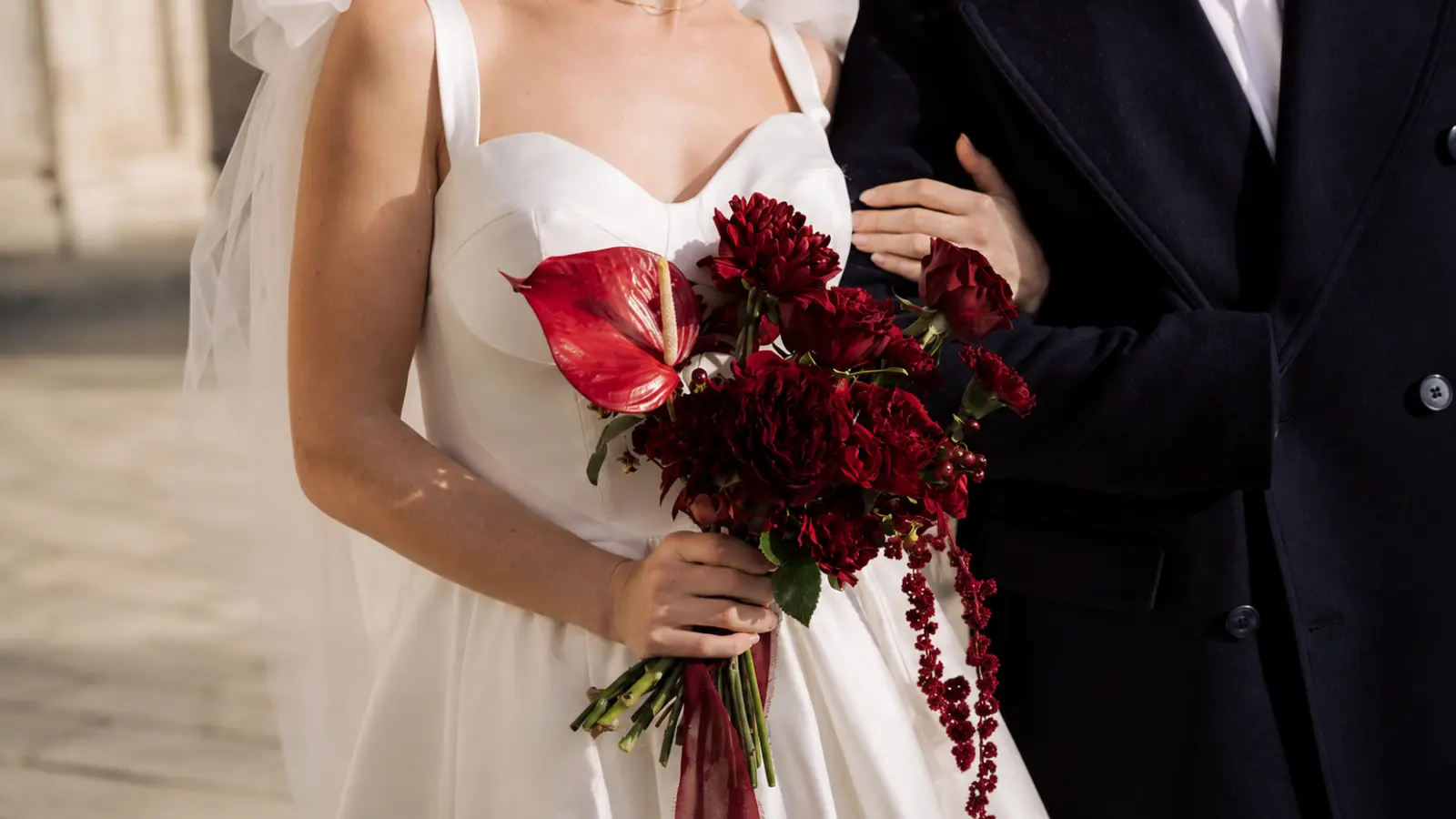 Bride holding a burgundy winter wedding bouquet with red anthurium, roses and rich seasonal flowers