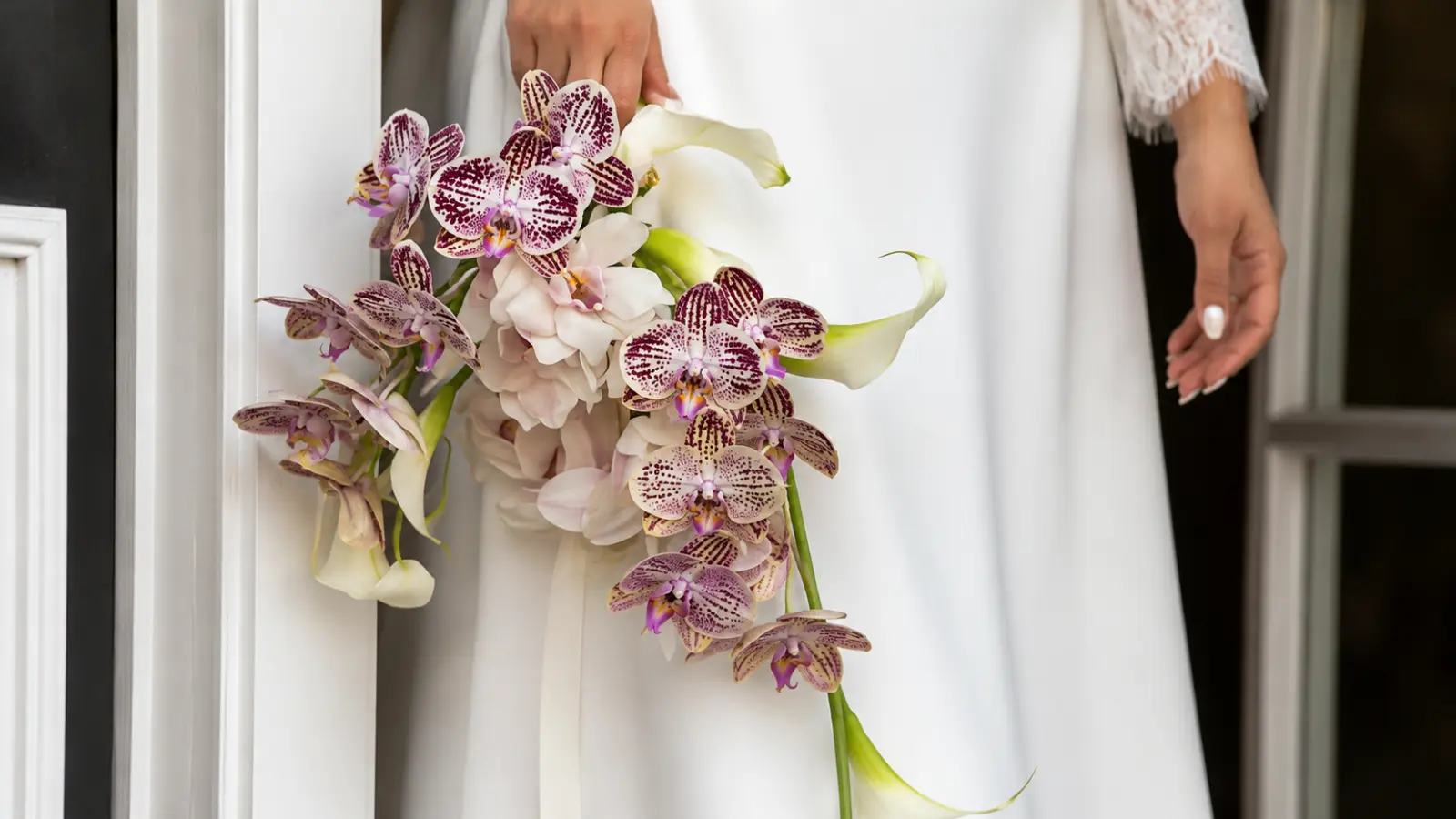 Bride holding a cascading bouquet with patterned phalaenopsis orchids, white calla lilies, and blush garden roses