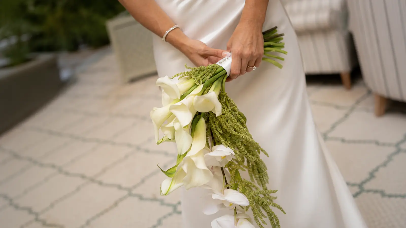 Bride holding a cascading wedding bouquet featuring white calla lilies, orchids, and flowing green amaranthus