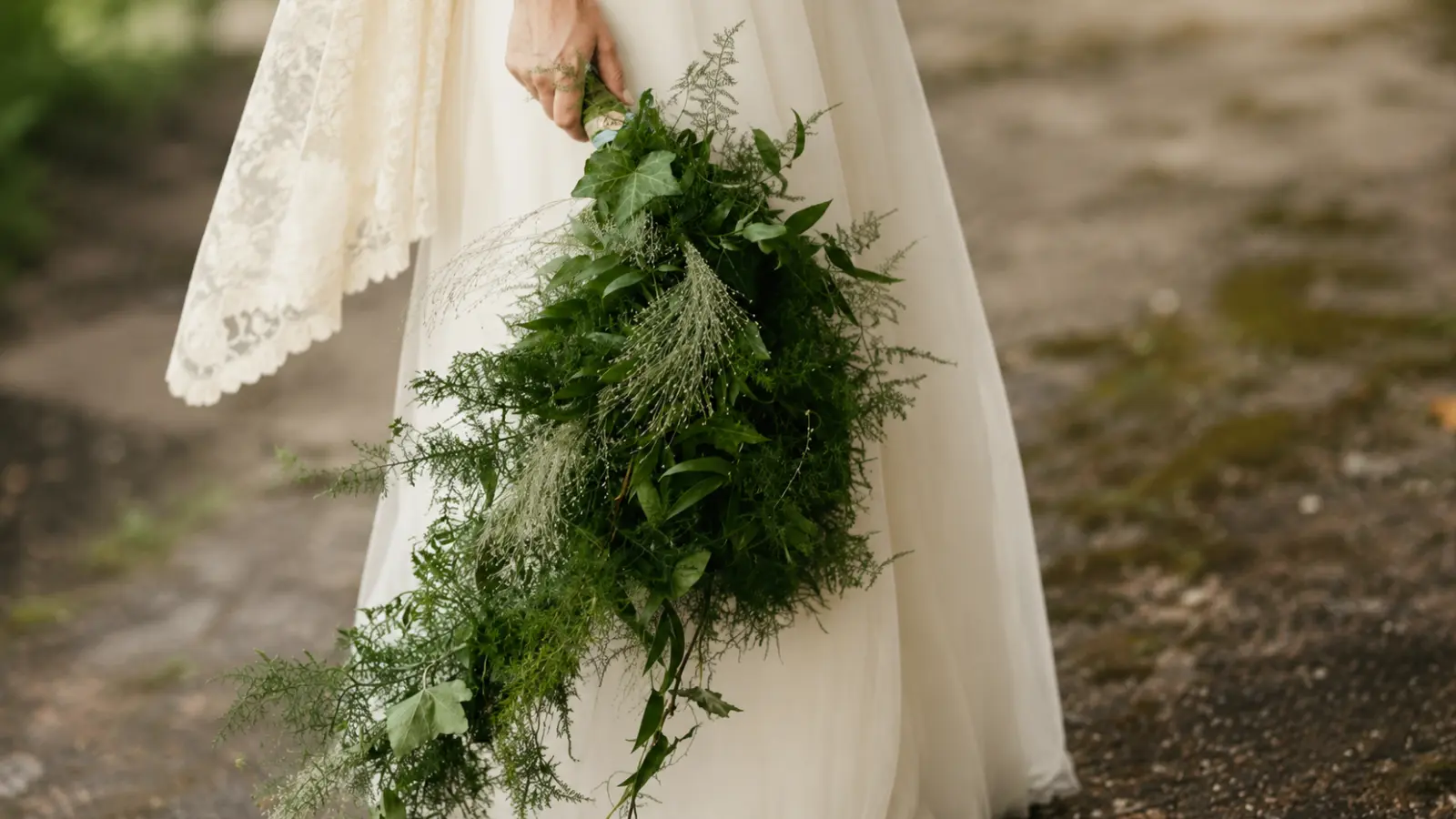 Bride holding a cascading greenery winter wedding bouquet with ivy and flowing evergreen foliage