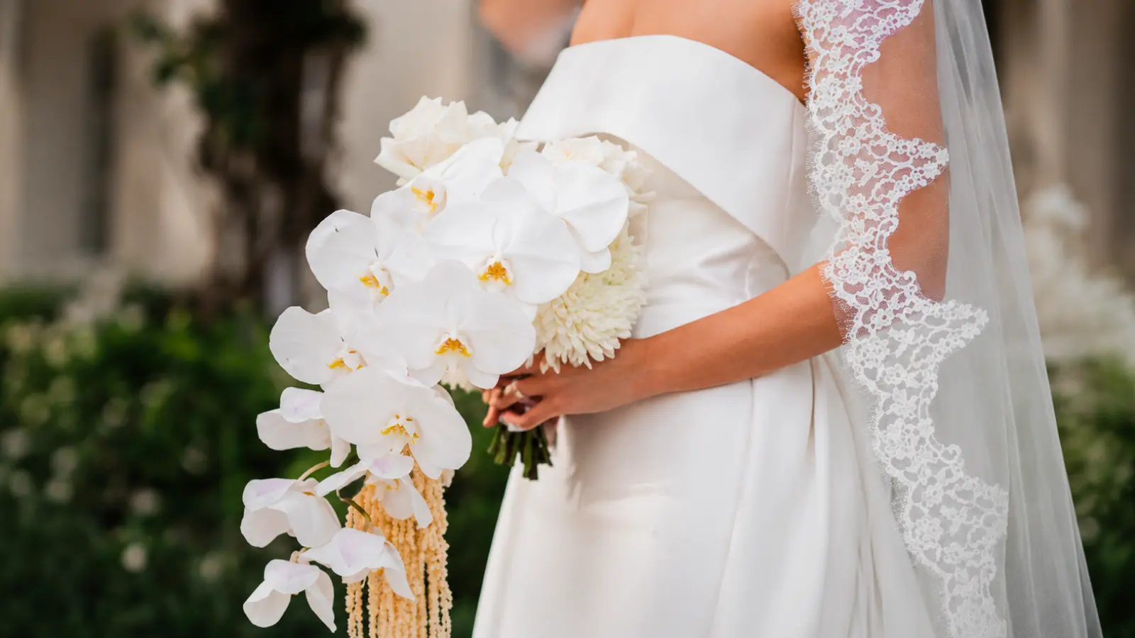 Bride holding a cascading bouquet with white phalaenopsis orchids, white calla lilies, and trailing amaranthus