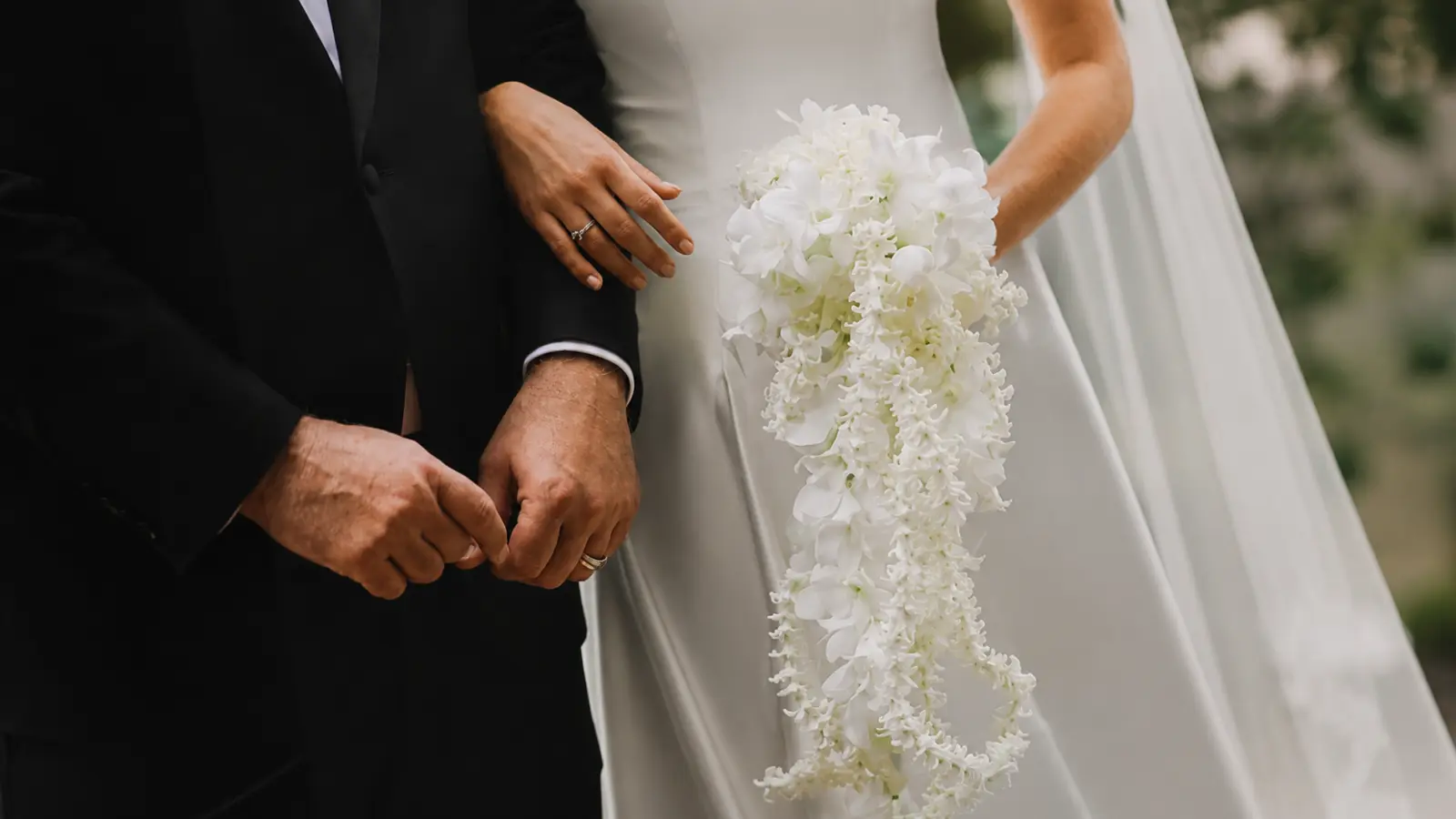 Bride holding a cascading white orchid wedding bouquet with elegant trailing flowers