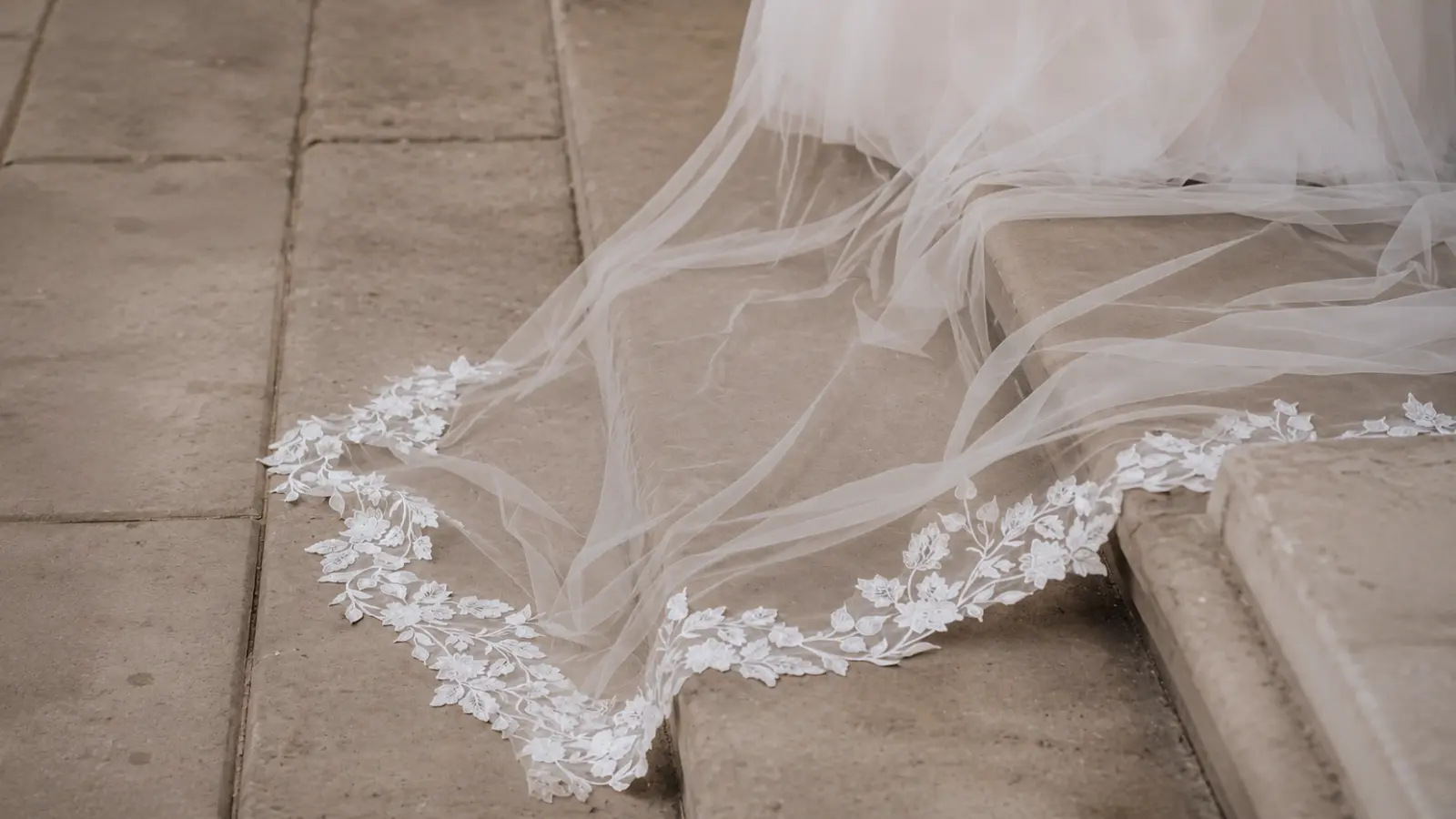 Close-up of a cathedral wedding veil train with floral lace appliqués flowing across stone steps