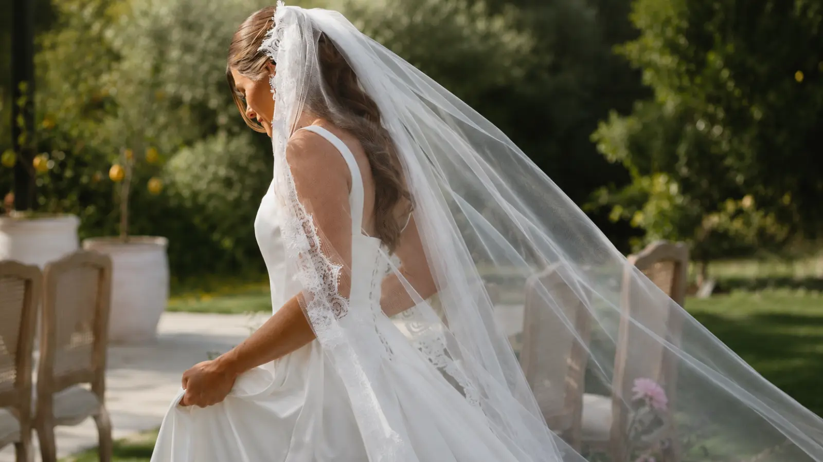 Bride walking outdoors in a satin wedding dress with a flowing cathedral wedding veil trimmed with lace