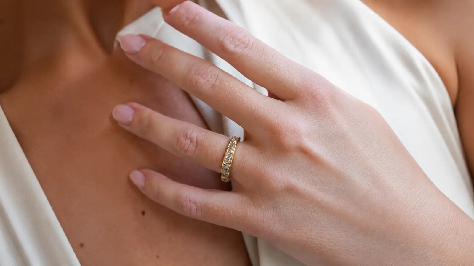 A hand wearing a classic channel set wedding band in yellow gold featuring a row of subtle diamonds across the band