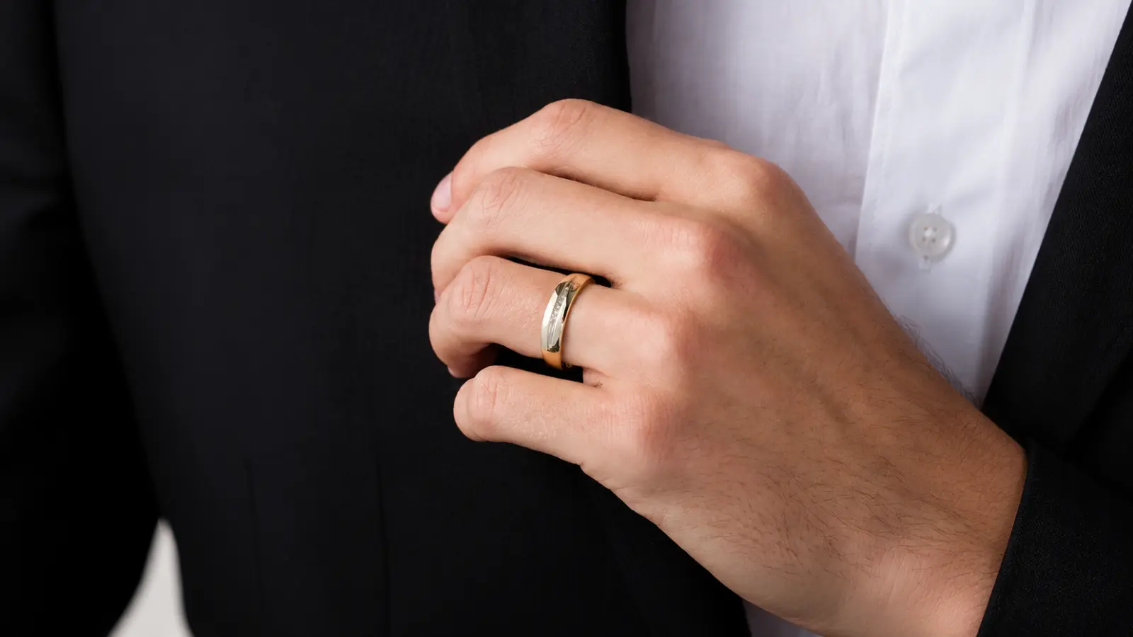 Close-up of a groom wearing a classic men's diamond wedding band with a polished gold finish and subtle diamond accents