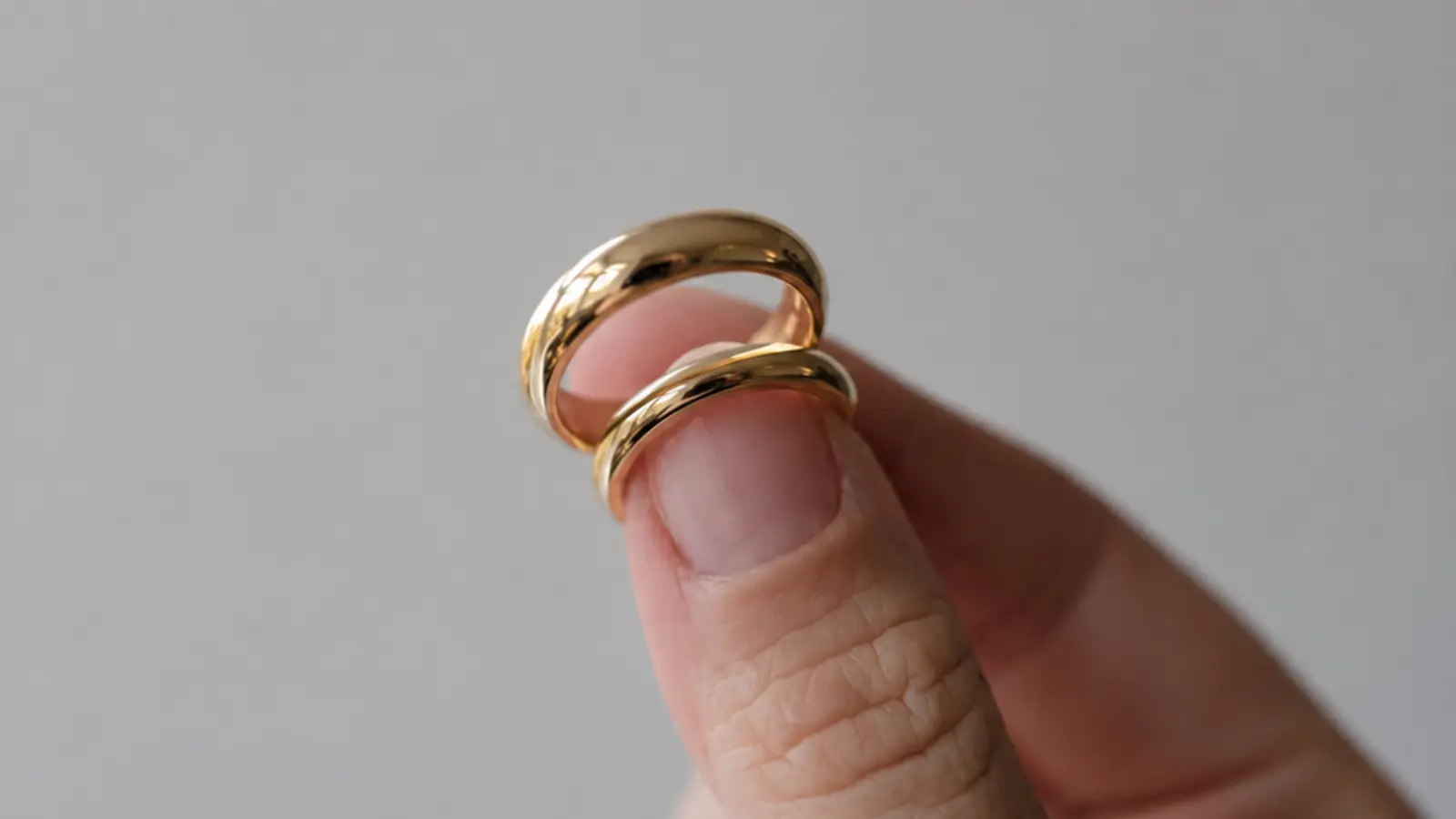 Two polished minimalist yellow gold wedding bands held between fingers, showcasing clean lines and timeless everyday elegance