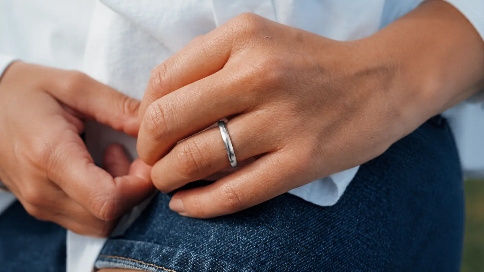 A close-up of a hand wearing a polished platinum wedding ring, showcasing its naturally white appearance, smooth finish and timeless minimalist design for everyday wear