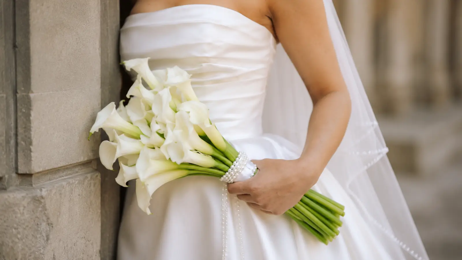 Bride holding a classic white calla lily wedding bouquets wrapped with white satin ribbon and pearl accents