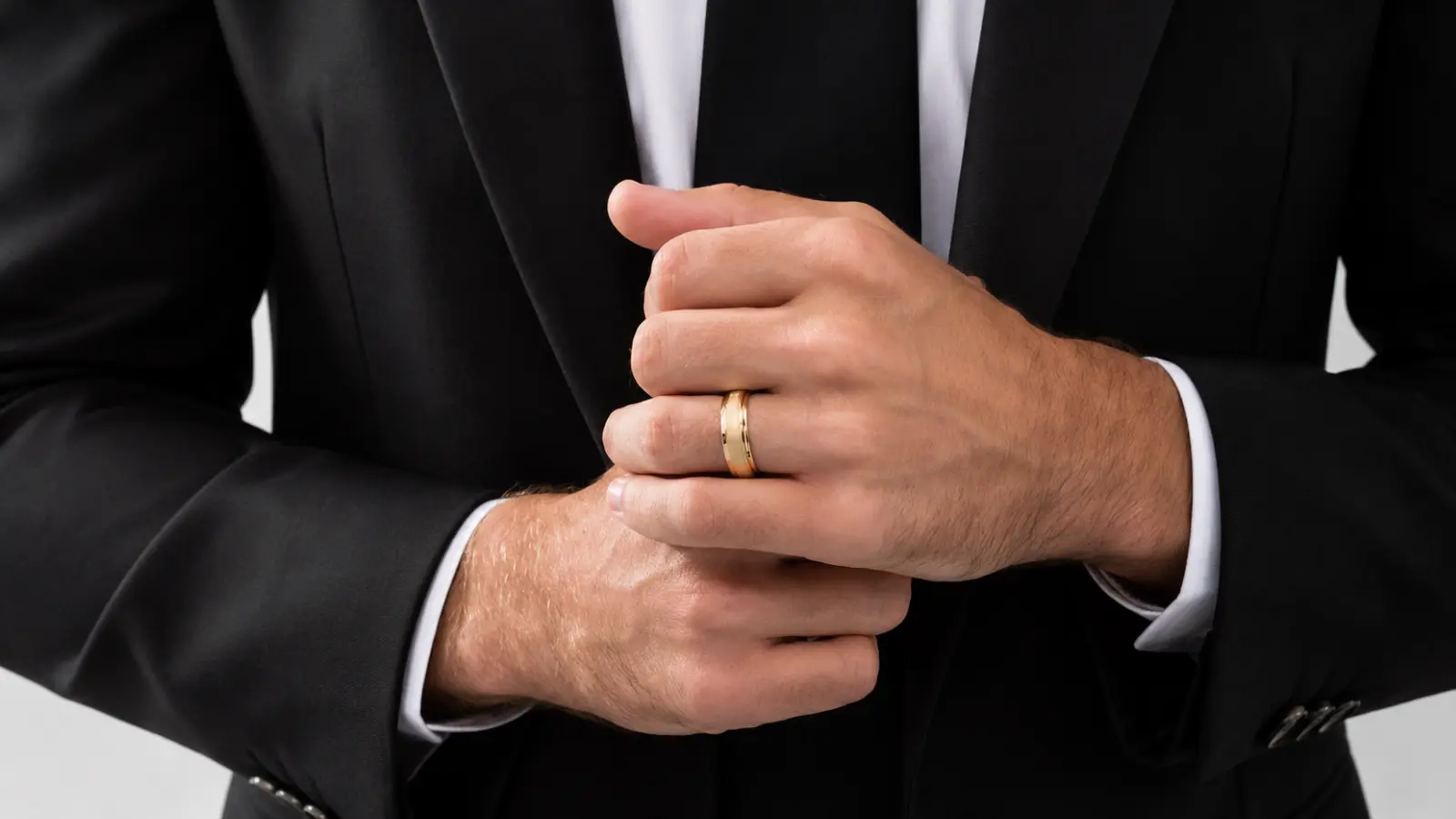 Groom fastening a gray suit jacket while wearing a polished yellow gold men's wedding band with a classic rounded profile and timeless design