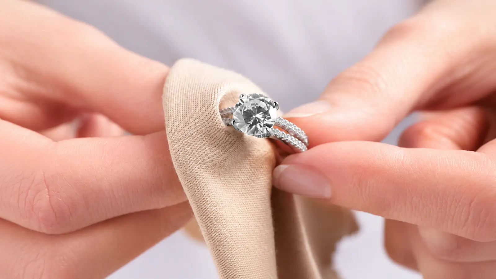 Hands drying and polishing a diamond engagement ring with a soft jewelry cloth after gentle cleaning