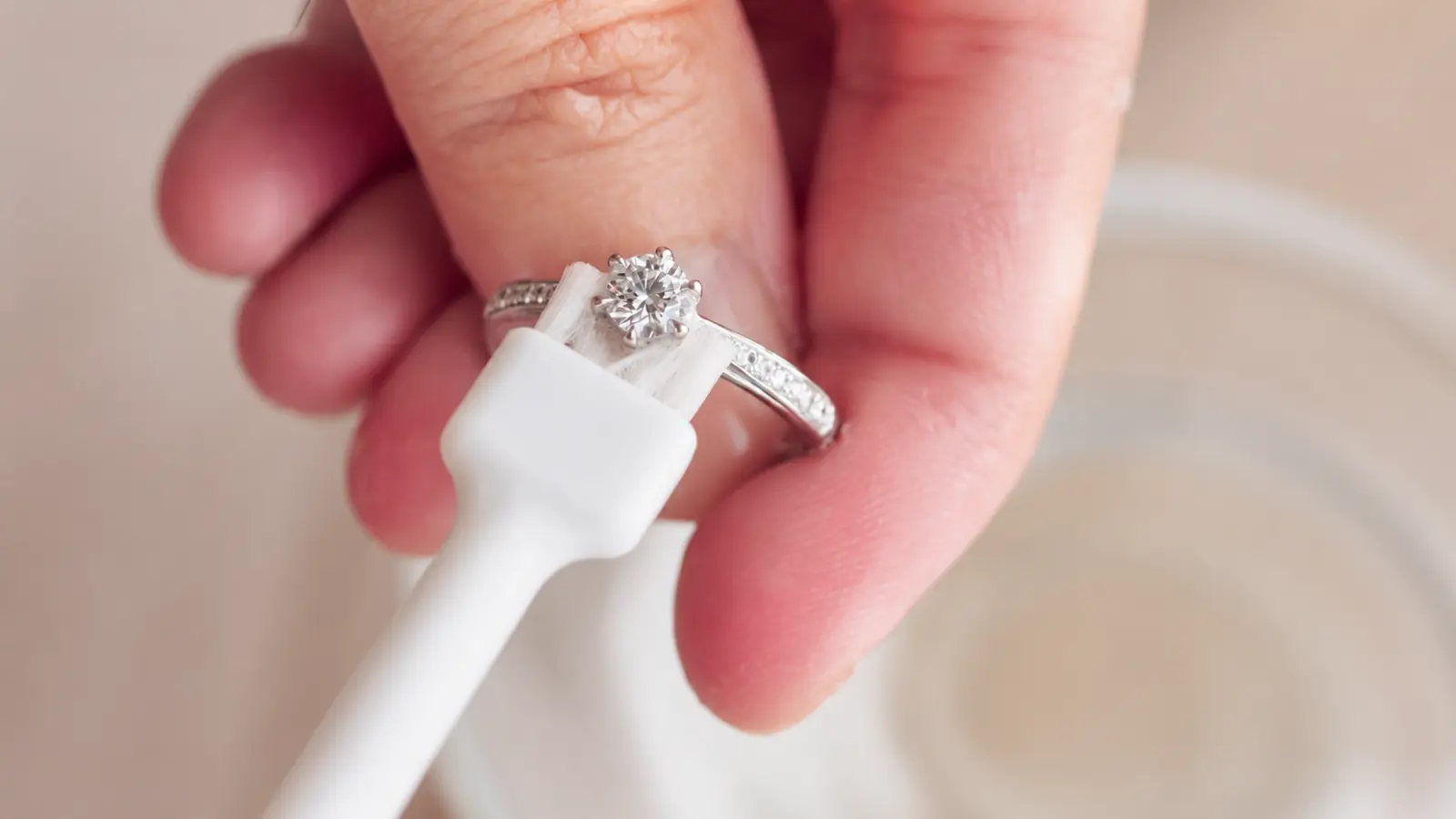 A soft toothbrush cleaning around a diamond engagement ring setting to safely remove dirt and residue
