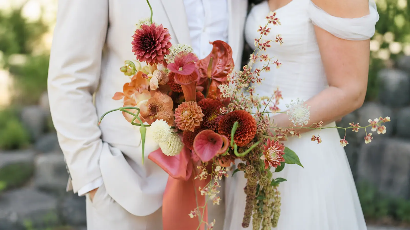 Bride and groom posing with a colorful cascading wedding bouquet featuring coral peach blush and ivory flowers