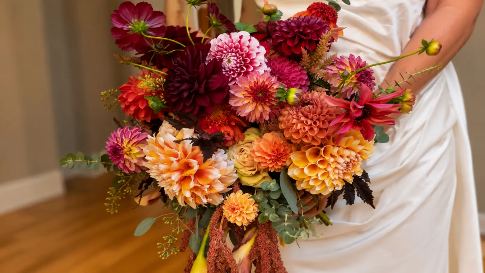 Bride holding a colorful fall wedding bouquet with dahlias, chrysanthemums and vibrant autumn flowers