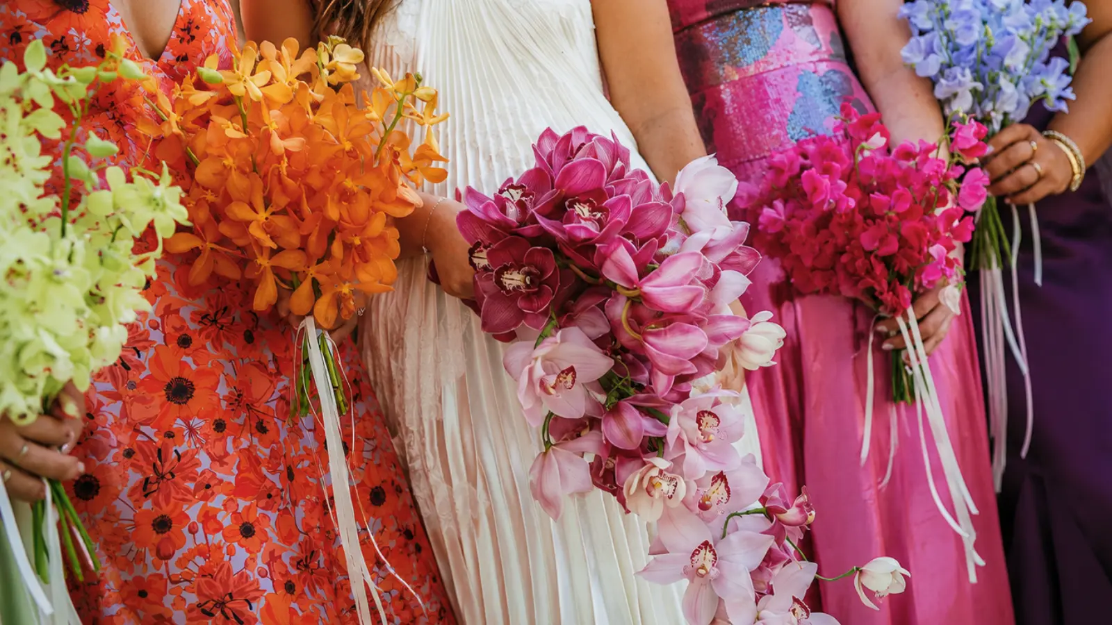 Bridesmaids in colorful dresses holding bright orchid wedding bouquets