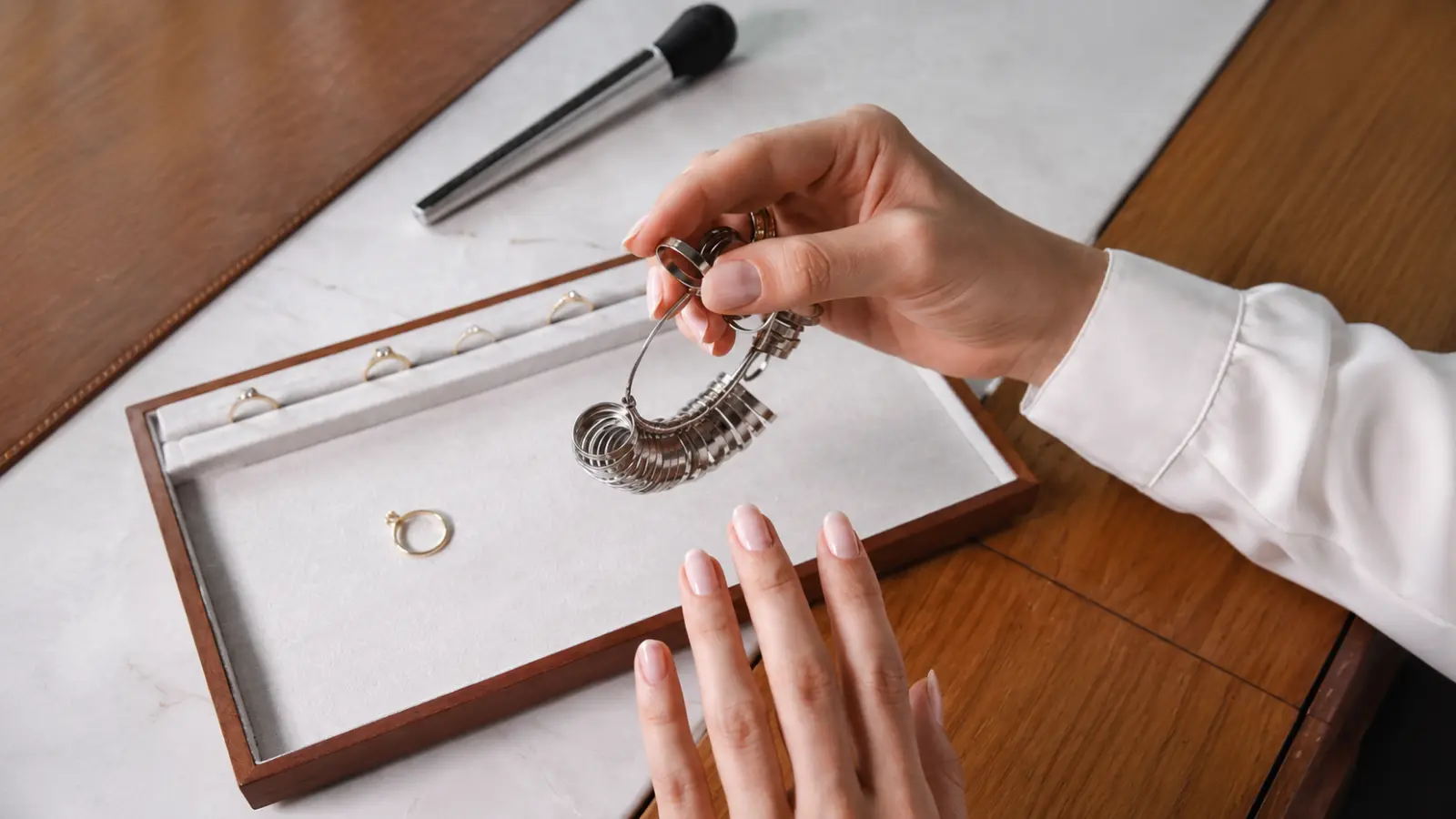 A person holding a professional ring gauge set while comparing different wedding ring sizes on a jewelry display tray