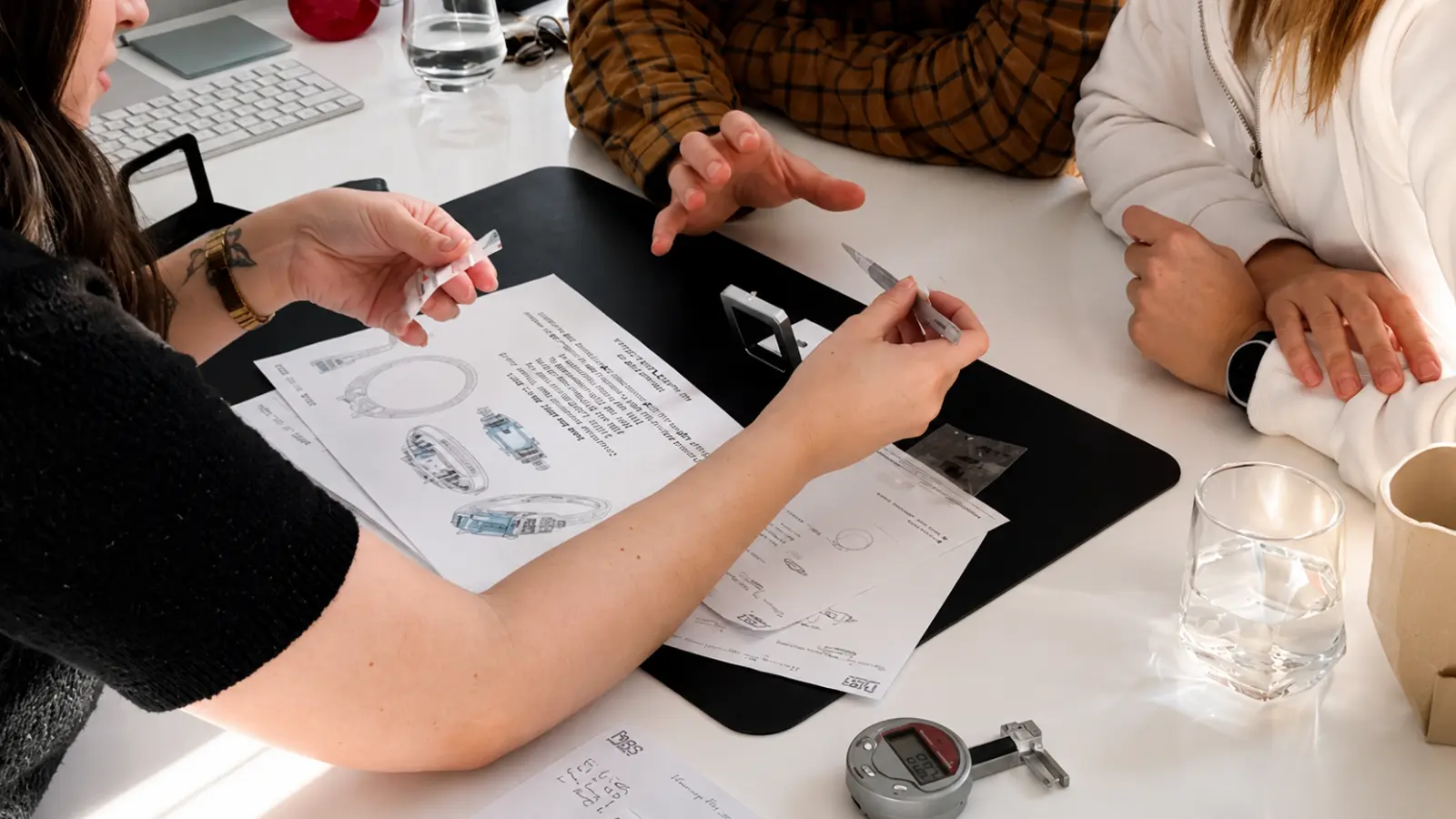 A couple consulting with a jewelry designer about a custom wedding ring upgrade, reviewing ring designs, diamond options, settings, measurements, and personalized customization choices before production begins