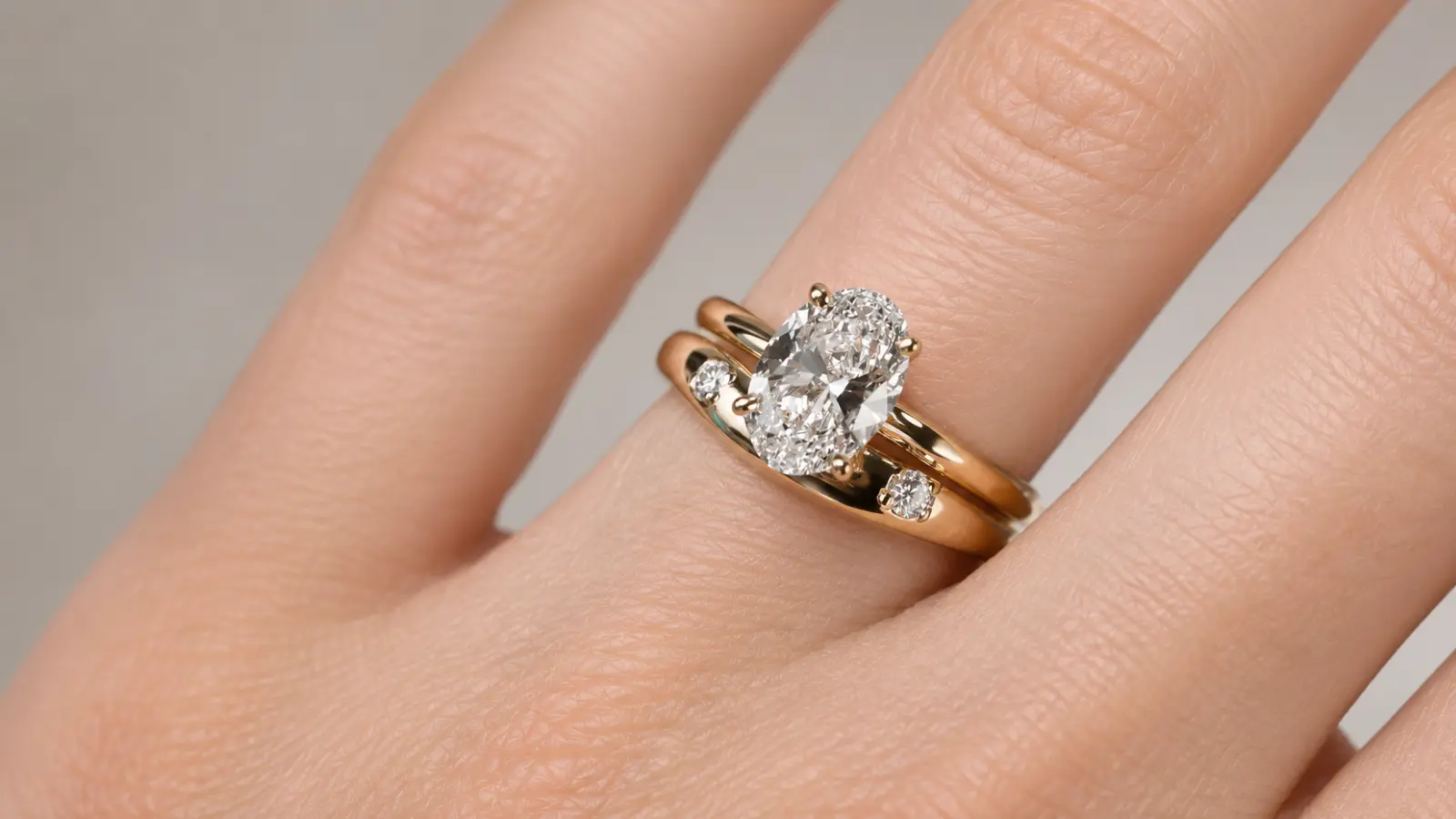 A close-up of a curved bridal ring wrap surrounding an oval diamond engagement ring with polished yellow gold bands