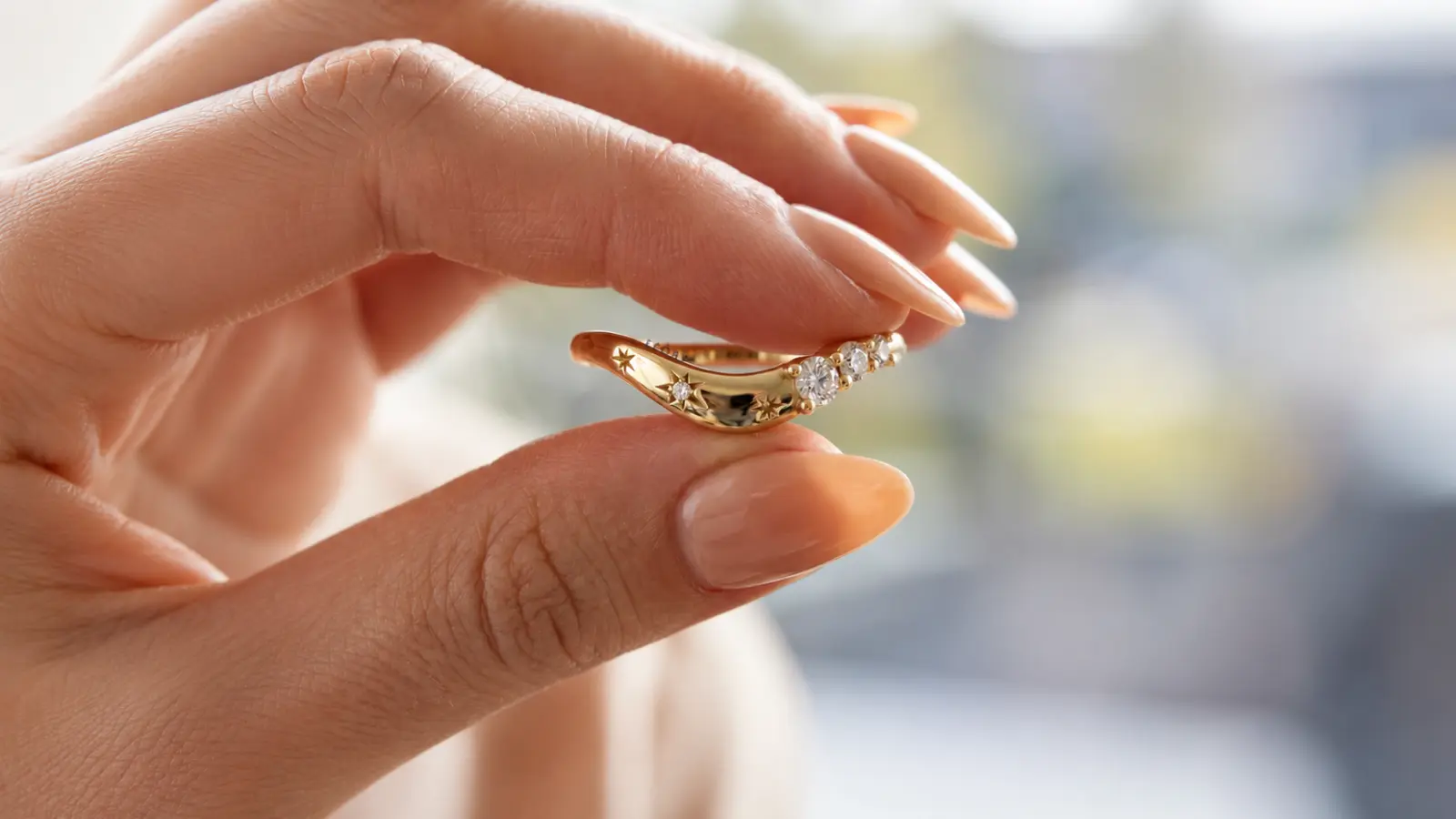 A hand wearing a curved solitaire engagement ring with a round diamond set on a flowing yellow gold band