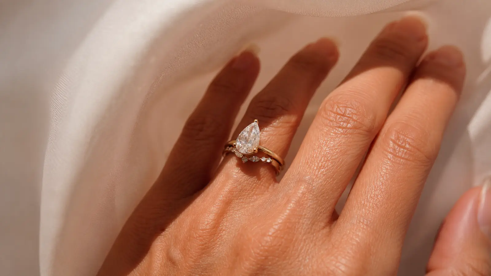 A curved wedding band sitting closely beneath a pear shaped engagement ring for a flush bridal stack