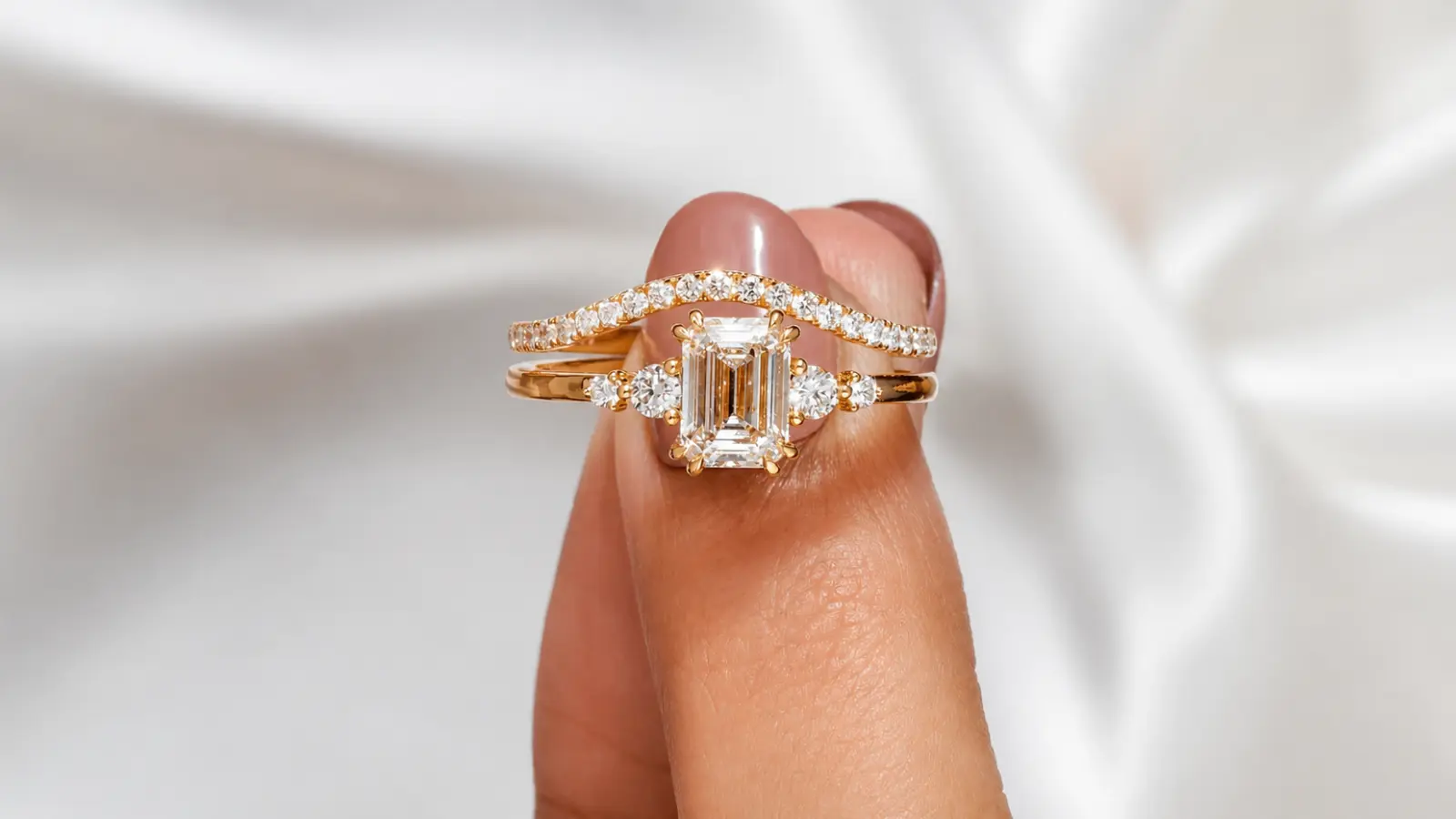 A curved diamond wedding band paired with an emerald cut engagement ring in a modern bridal stack