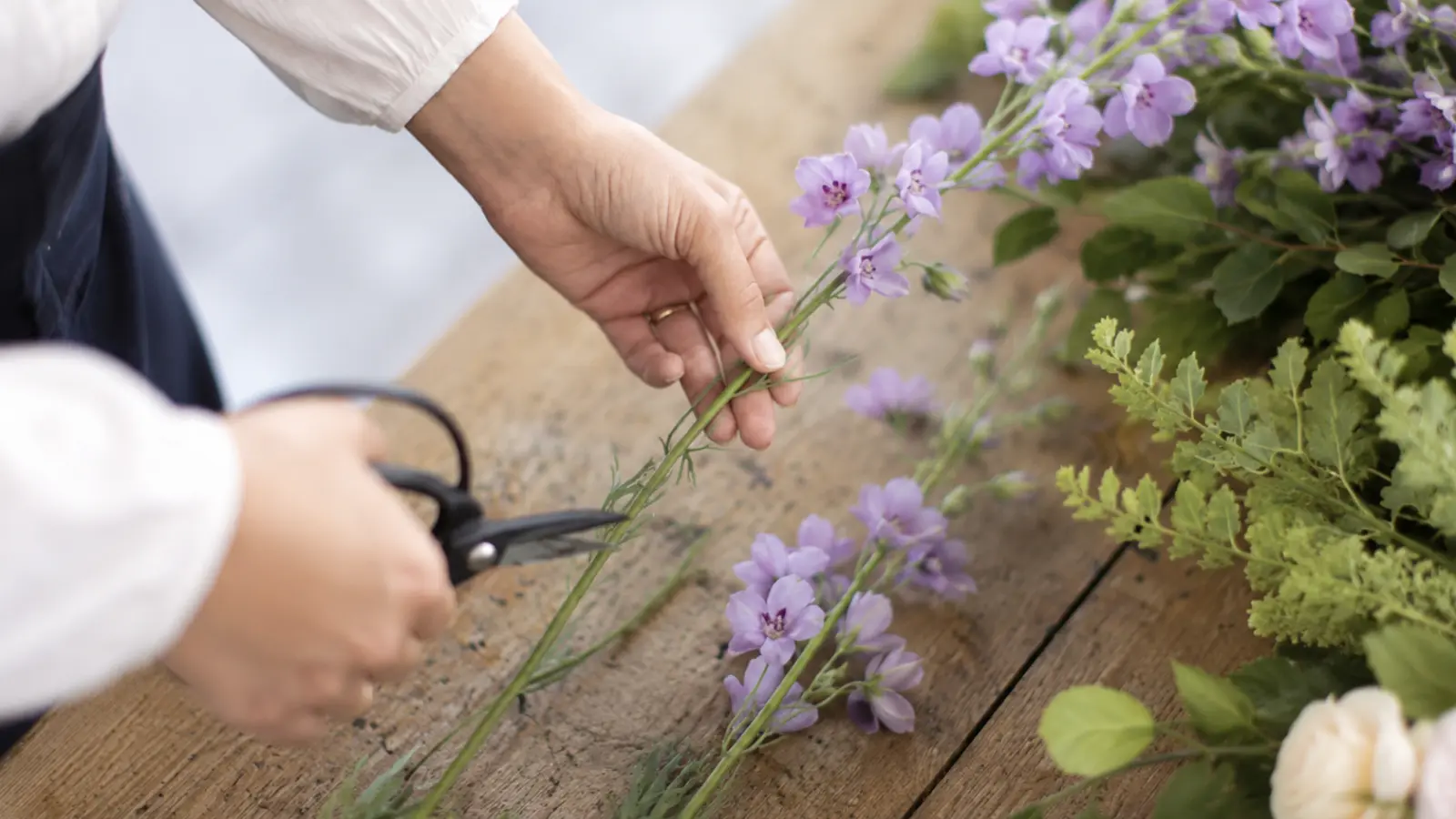 Florist trimming fresh lavender flowers while preparing a purple wedding bouquet
