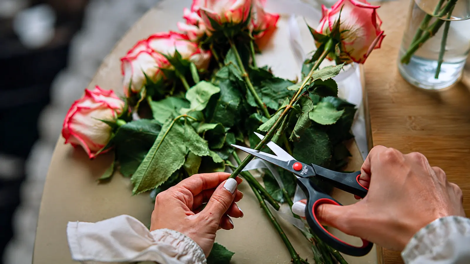 Hands cutting the stems of fresh roses with floral scissors while preparing flowers for a wedding bouquet