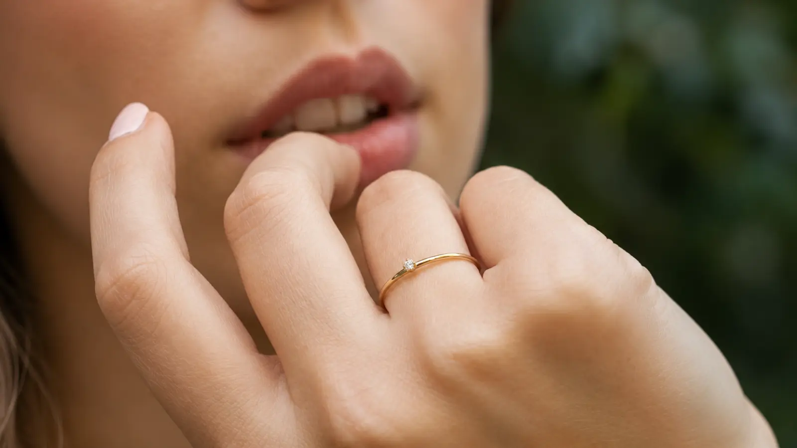 A close-up of a hand wearing a dainty minimalist wedding ring featuring a tiny solitaire diamond on a slim gold band