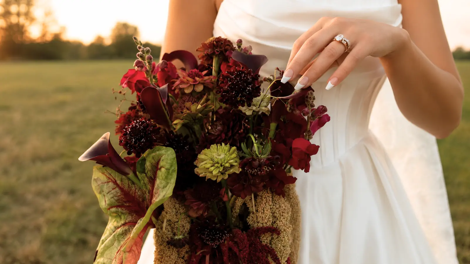 Bride arranging a dark burgundy cascading wedding bouquet with calla lilies and rich autumn flowers