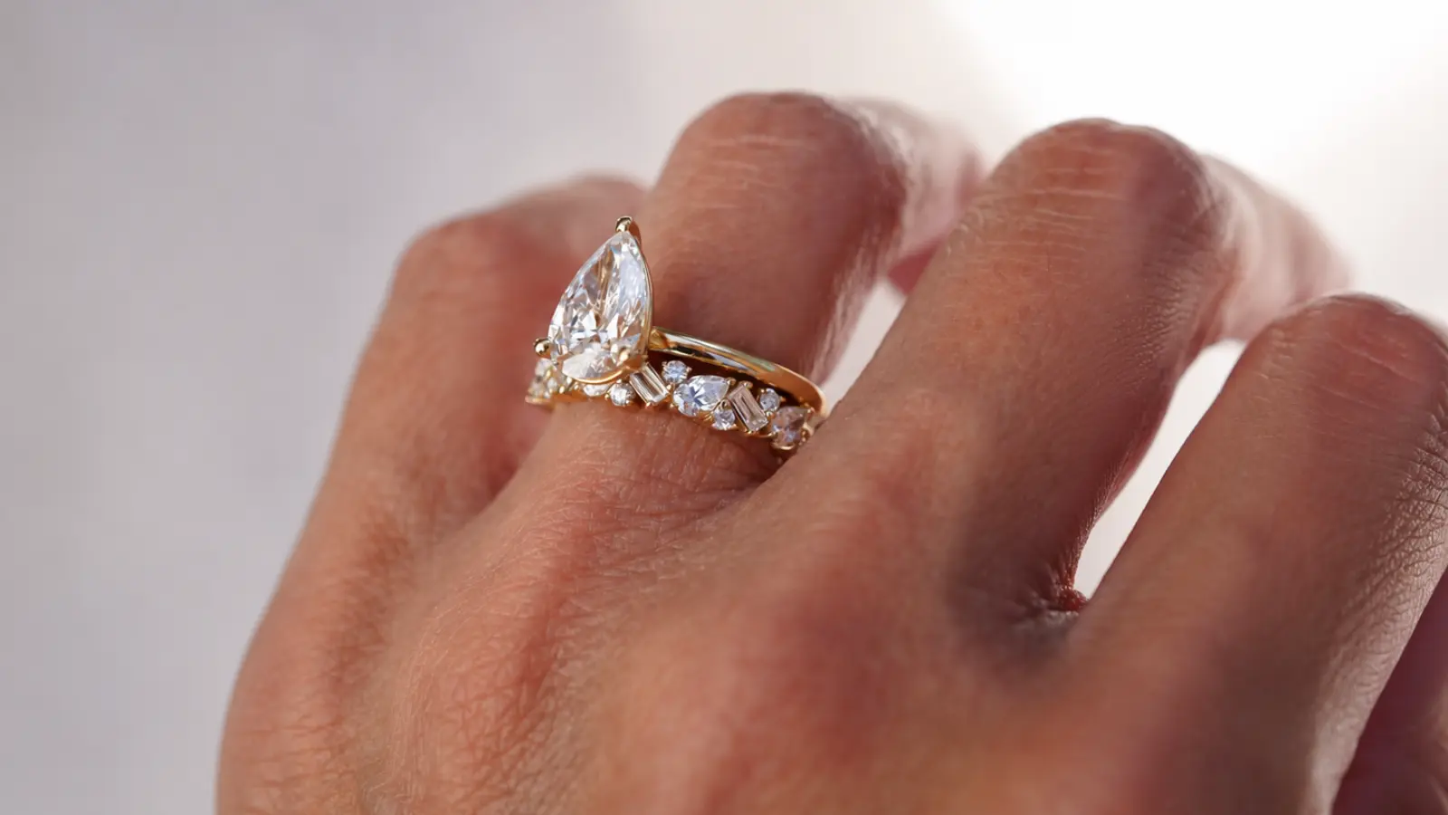 A pear shaped engagement ring paired with a decorative diamond wedding band in an elegant bridal stack