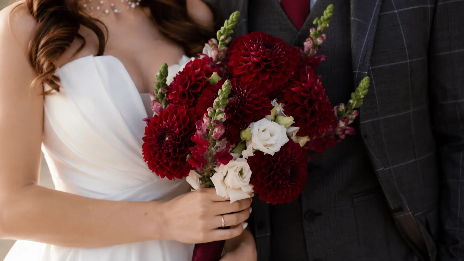Bride holding a deep red dahlia wedding bouquet accented with white roses and burgundy flowers