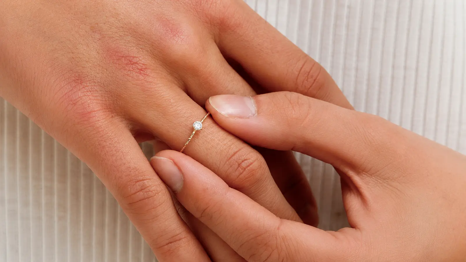 A delicate yellow gold solitaire engagement ring with a round diamond is gently placed onto a bride's finger, showcasing a timeless minimalist design with refined and elegant proportions