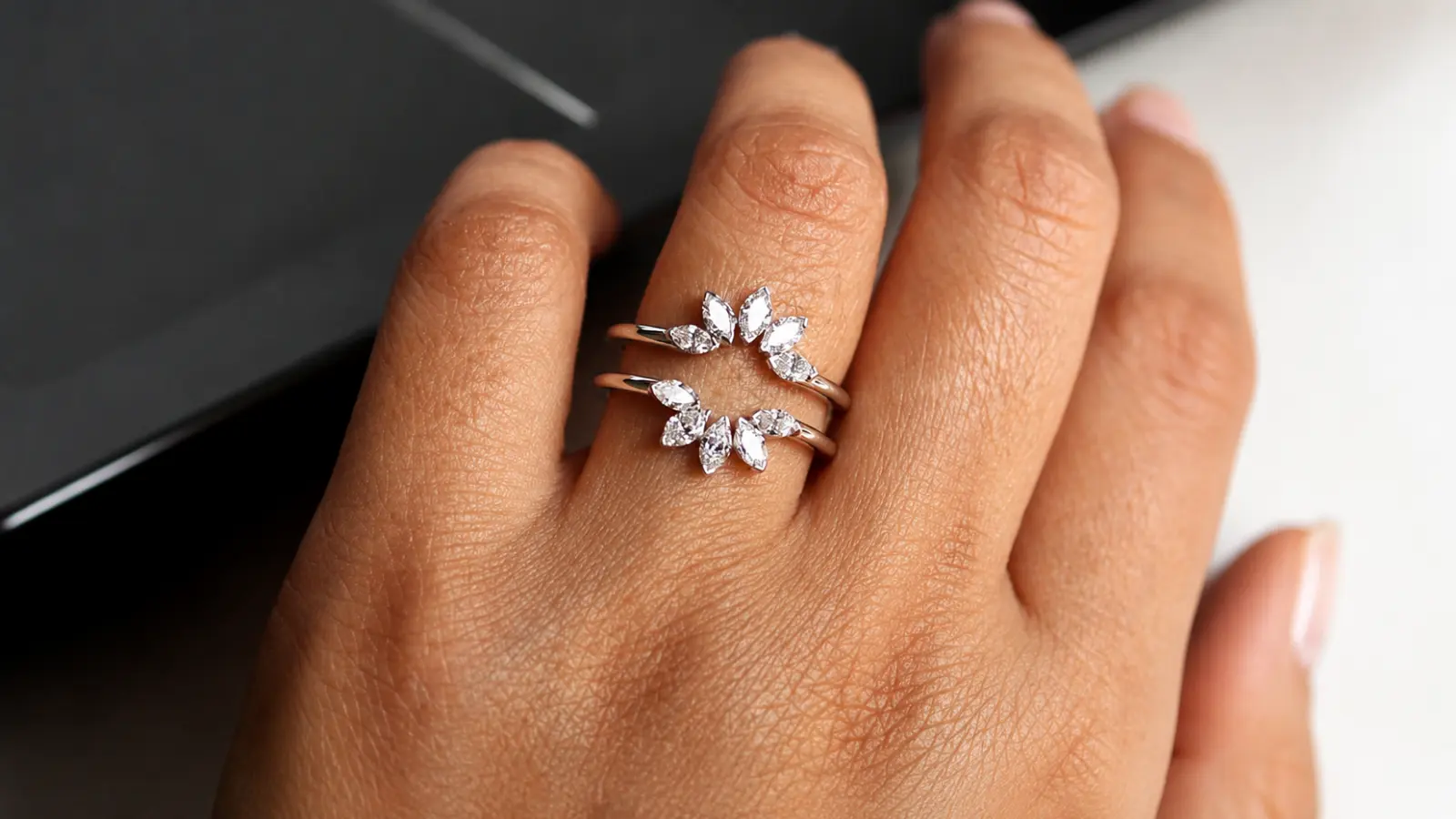 A floral-inspired diamond ring guard with marquise and round diamonds wrapped around an engagement ring on a woman's hand