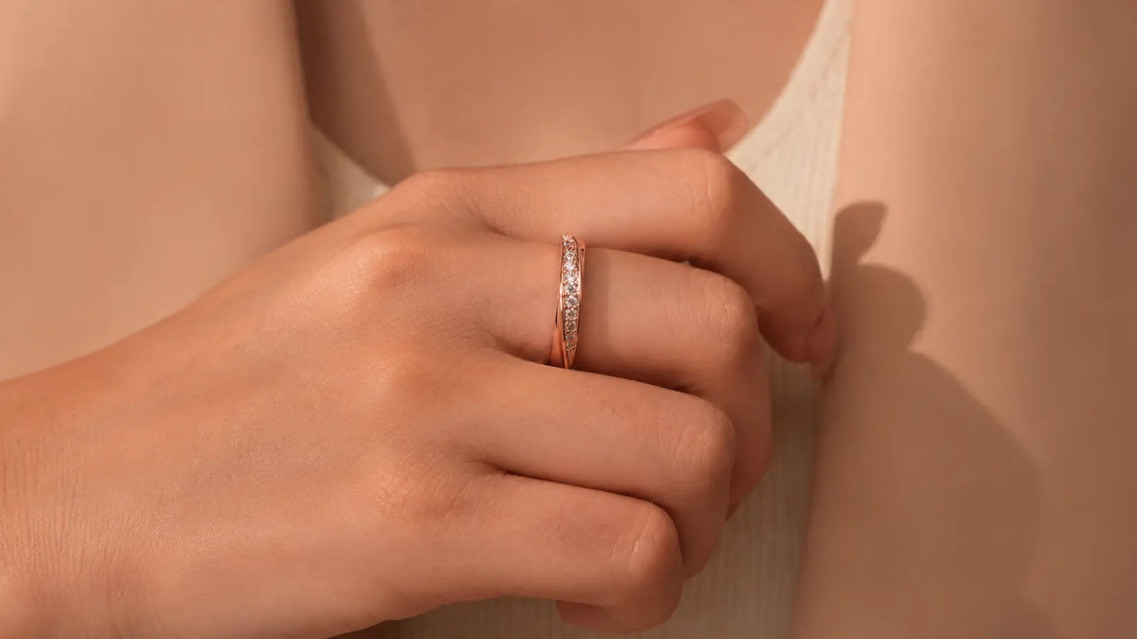 A bride wears a slim rose gold wedding ring accented with sparkling diamonds, showcasing its refined design, feminine style and warm romantic color against soft natural light
