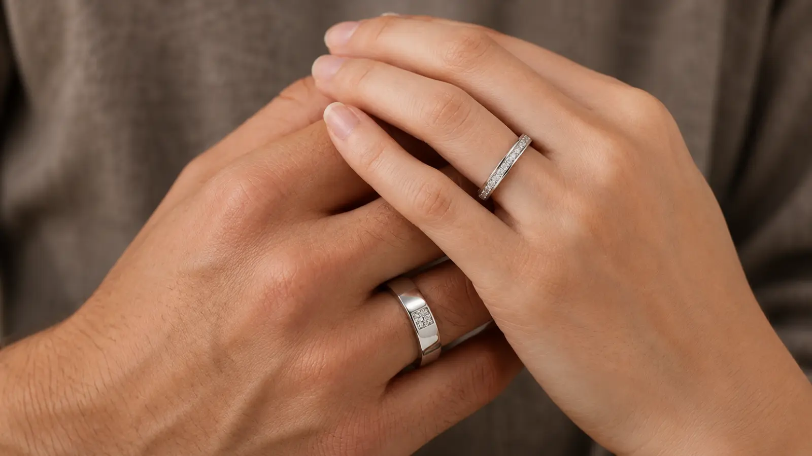 Two hands display matching diamond wedding bands featuring refined diamond accents and polished metal finishes in a coordinated couple's design