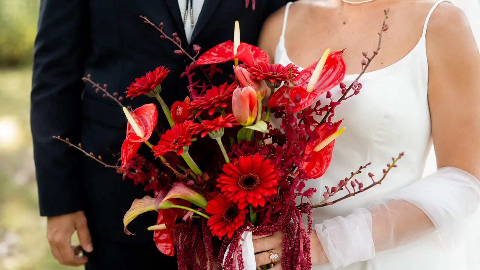 Bride holding a dramatic red and burgundy wedding bouquets with glossy anthuriums, red gerberas and cascading amaranthus